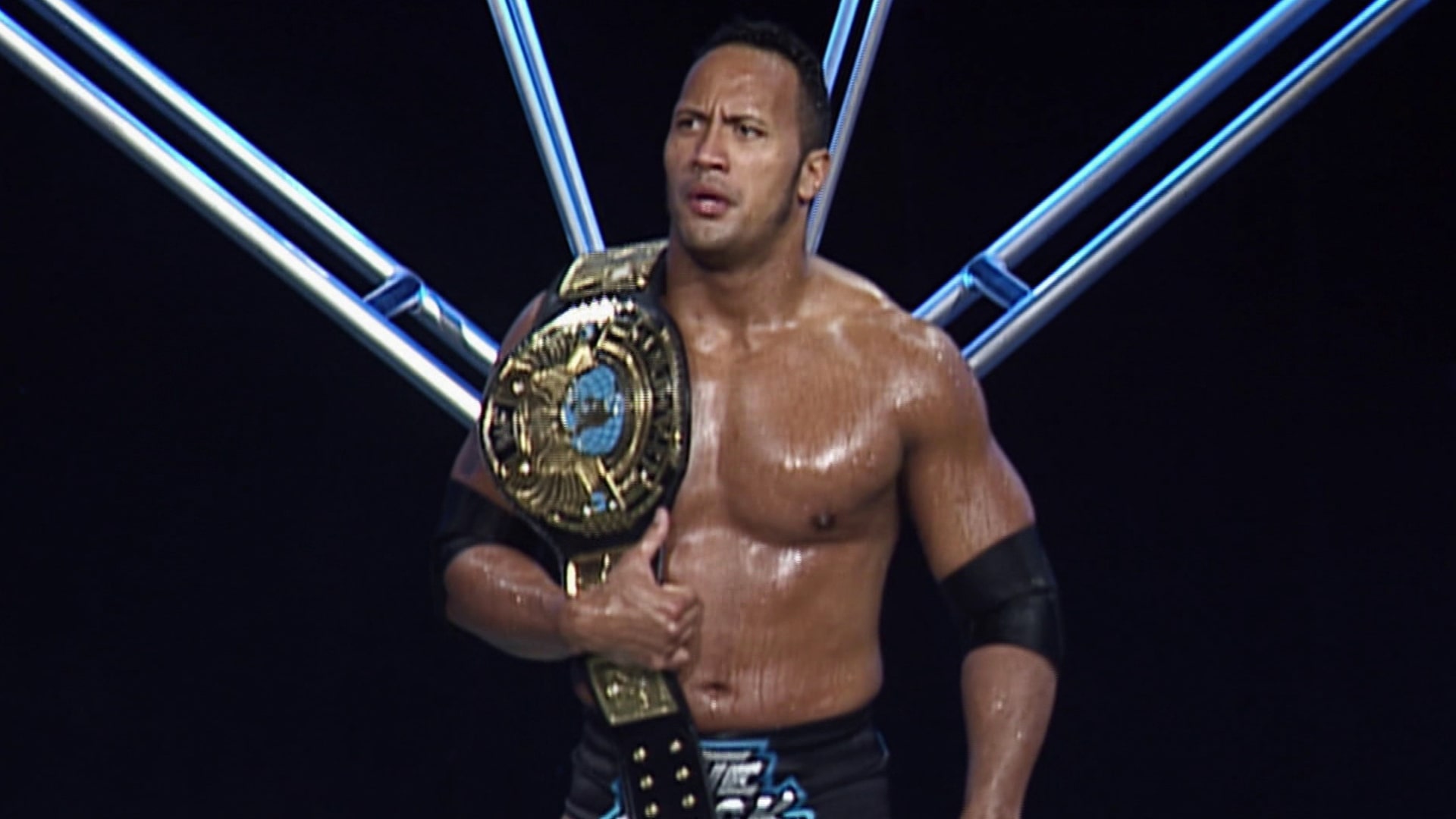 The Rock standing with a belt over his shoulder