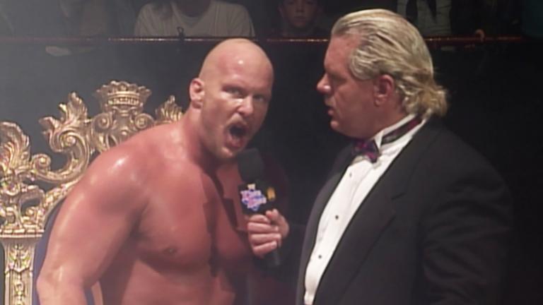 Steve Austin looks at the camera as he talks aggressively into a microphone held by the announcer
